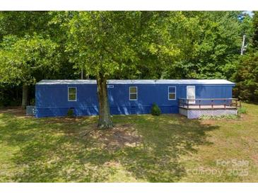 A mobile home with a blue exterior and a small porch surrounded by lush greenery and trees at 41042 Dennis Rd, Albemarle, NC 28001