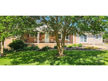Inviting single-story brick home with a cozy porch and charming curb appeal, surrounded by mature trees and lush landscaping at 116 Woodbark Ln, Kings Mountain, NC 28086