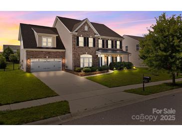 Charming brick two-story home with a manicured lawn and attached two-car garage at twilight at 9937 Violet Cannon Nw Dr, Concord, NC 28027