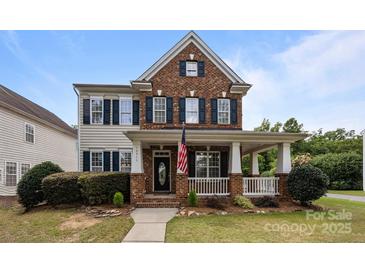 Charming two-story brick home with a welcoming front porch and manicured lawn and a visible American flag at 10349 Alvarado Way, Charlotte, NC 28277