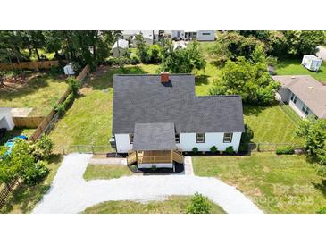 Aerial view of a home with a gray roof, white siding, front porch, gravel driveway, and a fenced in front and side yard at 307 W Sunset Dr, Moore, NC 28110