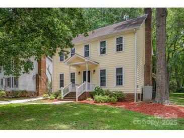 Charming two-story yellow home featuring a welcoming front porch and a lush, landscaped yard with mature trees at 10606 Danesway Ln, Cornelius, NC 28031