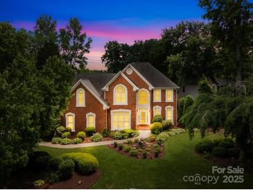 Elegant brick home with manicured lawn, lush landscaping, and warm, inviting exterior lighting at 9514 Hayenridge Ct, Huntersville, NC 28078