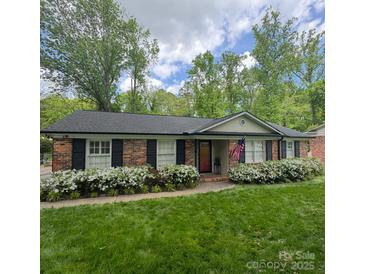 Charming brick home with black shutters and lush green lawn and beautiful white azalea bushes at 7026 Tabor Ln, Charlotte, NC 28211