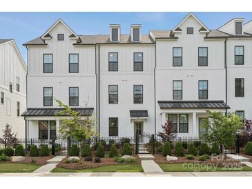 Charming exterior of a three-story white brick townhouse with manicured landscaping and a black iron fence at 4148 Alexander View Dr, Charlotte, NC 28226