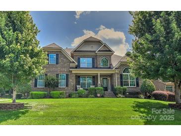 Brick two-story home with manicured lawn, lush trees and shrubbery under a blue sky with puffy white clouds at 3913 Widgeon Way, Waxhaw, NC 28173