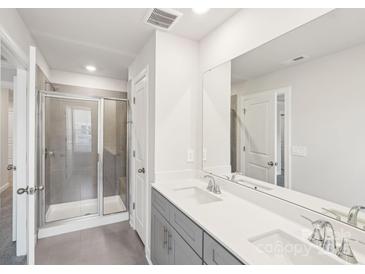 Bright bathroom featuring a glass shower, a dual sink vanity with gray cabinets, and large mirror at 135 Utility Ln, Mooresville, NC 28117