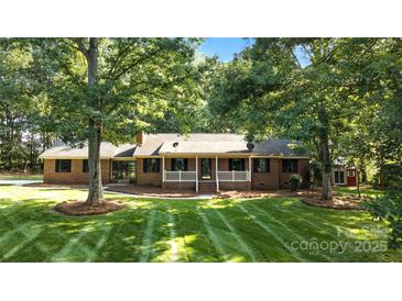 Charming brick home featuring a well-manicured lawn and covered porch nestled among mature trees at 4323 Crow Rd, Monroe, NC 28112