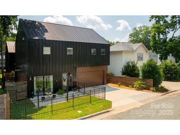 Modern black home with metal roof, garage, fenced yard, and patio seating area at 2107 W Trade St, Charlotte, NC 28216