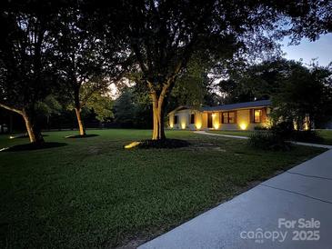 Charming home exterior featuring a spacious lawn, mature trees, and welcoming curb appeal at dusk at 209 Falcon Dr, Concord, NC 28025