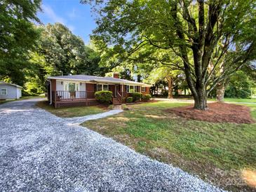 Charming brick home featuring a covered front porch, gravel driveway, and mature trees at 7812 Old Concord Rd, Salisbury, NC 28146