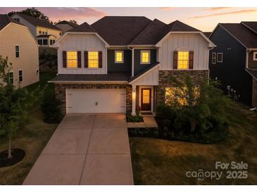 Charming two-story home featuring a stone facade, attached garage, and manicured lawn at dusk at 15119 Oleander Dr, Charlotte, NC 28278