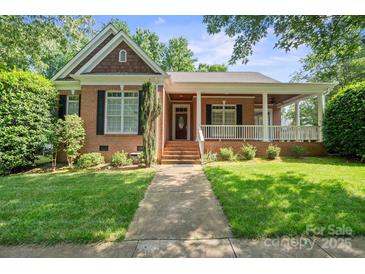 Charming brick home with a well-manicured lawn and inviting front porch, shaded by mature trees on a sunny day at 320 Magnolia St, Davidson, NC 28036