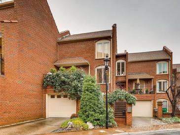 Charming brick townhome featuring lush landscaping, attached garage, and wrought iron gate at 311 Settlers Ln, Charlotte, NC 28202