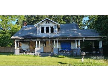 Exterior view of a house in poor condition with broken windows and boarded up doors, marked with caution tape at 619 N Main St, Landis, NC 28088