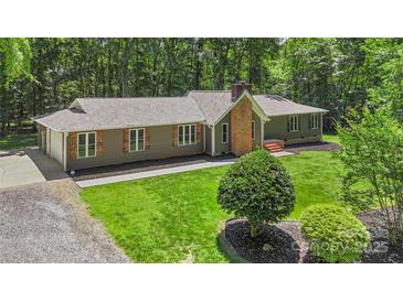 Ranch home featuring a brick chimney, shutters, and gravel drive, surrounded by mature trees on a well manicured lawn at 1556 Stanley Lucia Rd, Mount Holly, NC 28120