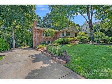 Charming brick home with lush landscaping, mature trees, and a long driveway on a sunny day at 5441 Wintercrest Ln, Charlotte, NC 28209
