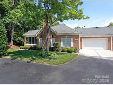 Brick home featuring a well-maintained front yard, attached garage, and a mature tree providing shade at 8465 Olde Troon Dr, Charlotte, NC 28277