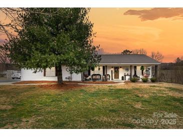 Charming home with covered front porch, decorative columns and metal roof on a large lot at sunset at 24253 Old Aquadale Rd, Albemarle, NC 28001
