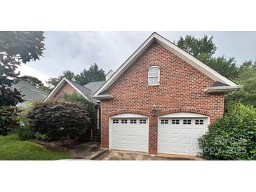 Red brick home featuring a two-car garage with white doors and mature landscaping at 1344 Moonshadow Ln, Shelby, NC 28150