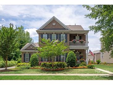 Charming two-story brick home featuring a double porch, lush landscaping, and an American flag at 10818 Alvarado Way, Charlotte, NC 28277