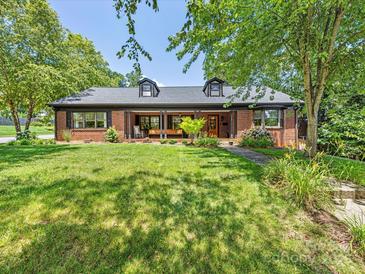 Charming brick home featuring a covered front porch,dormers, and mature trees in a lush green lawn at 112 8Th Nw Ave, Hickory, NC 28601