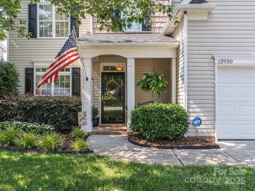 Charming home featuring a covered front porch with an American flag and lush landscaping at 13930 Daltrey Ln, Charlotte, NC 28277