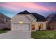 Charming white brick home featuring a three-car garage, complemented by a well-manicured lawn at dusk at 8163 Fairview Rd, Charlotte, NC 28226