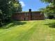 View of the rear exterior showing a brick facade, chimney, and large grassy backyard at 1111 S Skyland Dr, Mount Pleasant, NC 28124