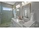 Bright bathroom featuring double sinks, quartz counters, tiled shower with glass door, and modern fixtures at 12119 Brooklyn Ave, Charlotte, NC 28204