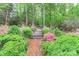 Lush garden with brick pathway leading to a wooden bridge, surrounded by flowering azaleas and mature trees at 715 Saint Cloud Dr, Statesville, NC 28625