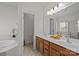 Bright bathroom featuring double sinks with wooden cabinets, soaking tub, and separate toilet room at 9341 Lenox Pointe Dr, Charlotte, NC 28273