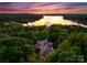 Aerial view of a lakeside home surrounded by mature trees with sunset reflection on the water at 10310 Wildlife Rd, Charlotte, NC 28278