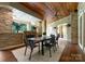 Inviting outdoor covered deck with a stone fireplace, wood ceiling, and dining set for alfresco enjoyment at 10310 Wildlife Rd, Charlotte, NC 28278