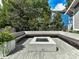 A backyard patio has light gray pavers, a concrete firepit, and benches with trees and bushes in the background at 2110 E 5Th St, Charlotte, NC 28204