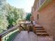 Spacious wooden deck and steps lead down from the brick house surrounded by lush, mature trees at 907 Weymouth Dr, Gastonia, NC 28056