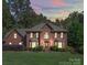 A brick home illuminated at dusk showcases its facade with symmetrical windows and manicured landscaping at 907 Weymouth Dr, Gastonia, NC 28056