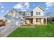 Two-story farmhouse features a front porch, attached two-car garage, and landscaped lawn at 7073 Stella Pl, Stanley, NC 28164