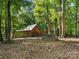 Exterior view of a wooden outbuilding, set amongst mature trees with a circular fire pit nearby at 13079 Philadelphia Church Rd, Oakboro, NC 28129