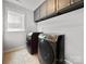 A laundry room featuring front-load washer/dryer, neutral tile, natural light and grey upper cabinets at 2657 Cheverny Pl, Concord, NC 28027