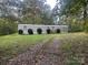 A single-level home featuring a gravel driveway lined with bushes and surrounded by lush trees at 1926 Scenic Dr, Iron Station, NC 28080