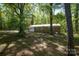 View of the rear brick home with white trim surrounded by mature trees in a wooded backyard at 1216 Stallion Ln, Lancaster, SC 29720