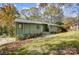 Green siding exterior shot of home in the woods on a sloped lawn in autumn at 11429 Spreading Oak Ln, Charlotte, NC 28226