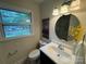 Well-lit bathroom featuring a round mirror, flowers, and a window with a view to the outside at 1727 Hartford Dr, Gastonia, NC 28052