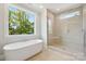 Elegant bathroom with a soaking tub, a glass shower, and a large window offering picturesque views at 15009 Brownleigh Ln # 26, Huntersville, NC 28078
