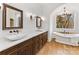 Elegant bathroom with dual sinks, a soaking tub, designer mirrors and lighting, and wood floors at 6040 Oxfordshire Rd, Waxhaw, NC 28173