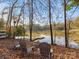 Lakeside relaxation with three chairs on a leaf-covered bank, offering a serene view of the calm lake and trees at 294 Carroll Cv, Clover, SC 29710