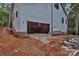 New construction with gray siding showing the open garage with brick foundation and surrounded by dirt and trees at 4615 Yellow Poplar Ln, Concord, NC 28025