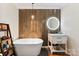 A bathroom featuring a soaking tub next to a wood-paneled accent wall and a modern, lighted round mirror at 946 Scotch Dr, Gastonia, NC 28054