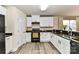 Well-lit kitchen with white cabinetry, modern appliances, black countertops, and sink with a view to the backyard at 7534 April Mist Trl, Huntersville, NC 28078